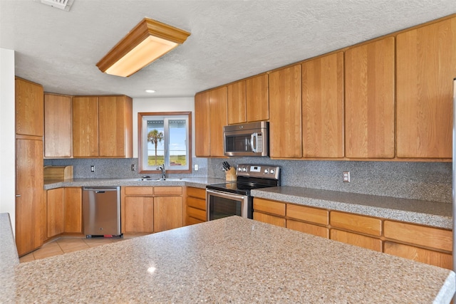 kitchen featuring backsplash, a sink, brown cabinetry, light tile patterned floors, and stainless steel appliances