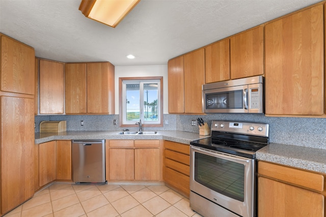 kitchen with appliances with stainless steel finishes, decorative backsplash, light stone counters, light tile patterned floors, and sink