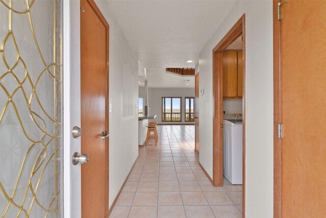 corridor with light tile patterned floors, washer / clothes dryer, and baseboards