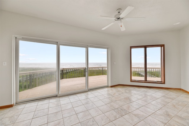 empty room with a water view, ceiling fan, and light tile patterned floors