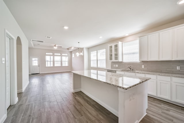 kitchen with white cabinets, backsplash, a center island, light stone countertops, and light hardwood / wood-style floors