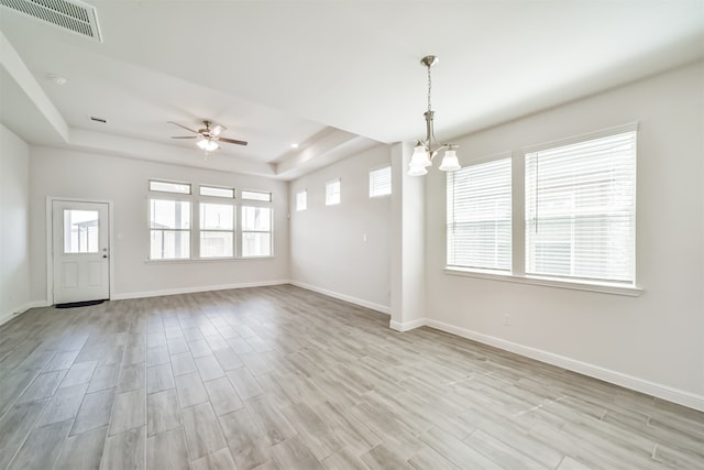 spare room with light wood-type flooring, ceiling fan with notable chandelier, a raised ceiling, and a wealth of natural light