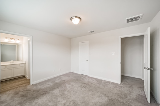 unfurnished bedroom featuring light colored carpet, a closet, connected bathroom, and sink