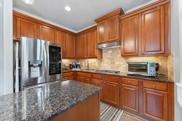 kitchen with appliances with stainless steel finishes, decorative backsplash, dark stone countertops, and crown molding