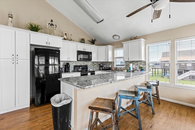 kitchen featuring light stone counters, a breakfast bar area, white cabinets, light hardwood / wood-style flooring, and black appliances