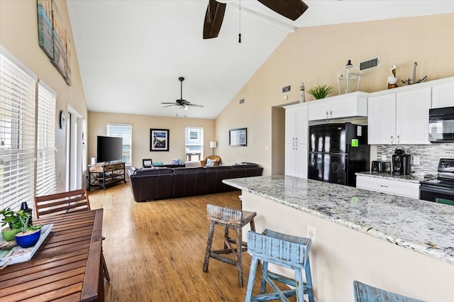 kitchen featuring a kitchen breakfast bar, white cabinets, high vaulted ceiling, light wood-type flooring, and black appliances