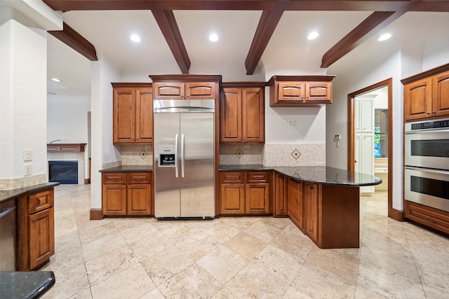 kitchen featuring appliances with stainless steel finishes, dark stone countertops, tasteful backsplash, kitchen peninsula, and beam ceiling