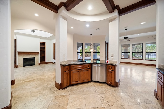 kitchen featuring dark stone counters, sink, hanging light fixtures, a fireplace, and stainless steel dishwasher