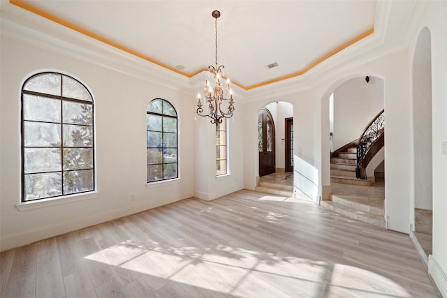 unfurnished dining area featuring an inviting chandelier, light wood-type flooring, a tray ceiling, and ornamental molding