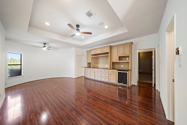 unfurnished living room featuring ceiling fan, beverage cooler, a tray ceiling, and dark hardwood / wood-style floors