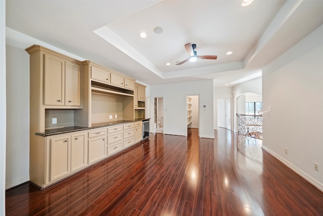 unfurnished living room featuring a tray ceiling, dark hardwood / wood-style floors, ceiling fan, and wine cooler