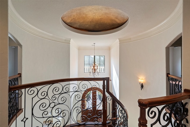 hall with a raised ceiling, crown molding, and a notable chandelier