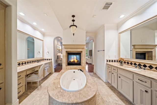 bathroom featuring decorative backsplash, vanity, a tiled fireplace, a bath, and ornamental molding