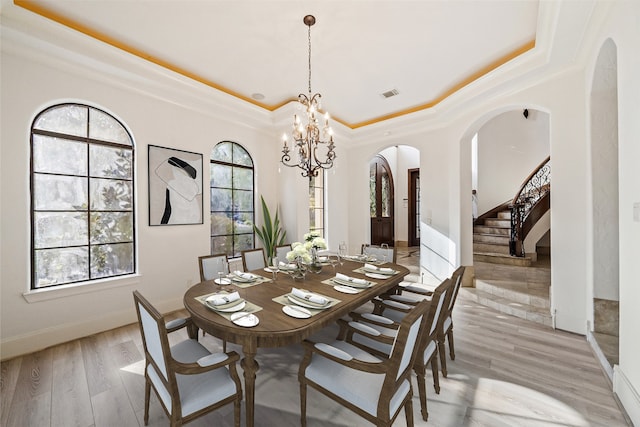 dining area featuring light hardwood / wood-style flooring, a raised ceiling, an inviting chandelier, and crown molding