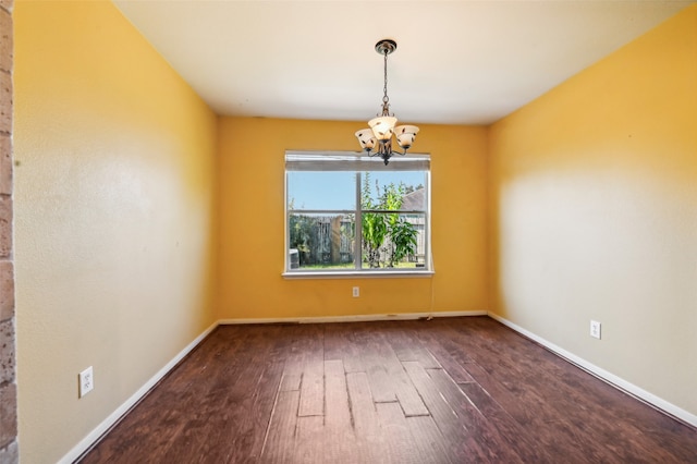 spare room with a notable chandelier and dark hardwood / wood-style flooring