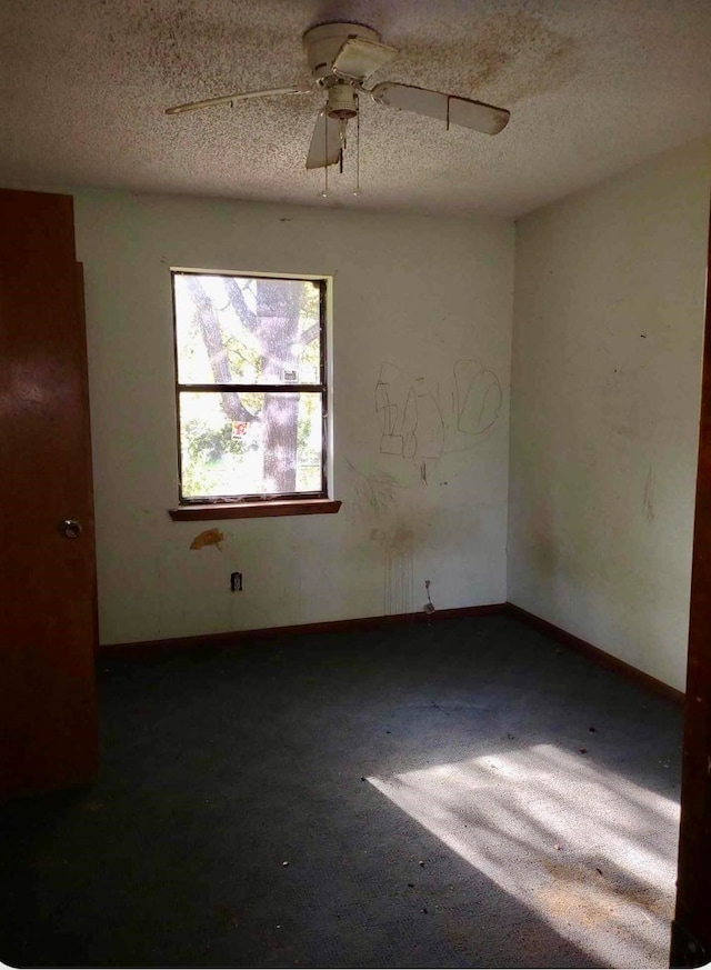 empty room with ceiling fan, a textured ceiling, and dark colored carpet