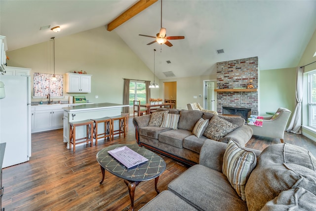 living room with dark wood-type flooring, high vaulted ceiling, ceiling fan with notable chandelier, a fireplace, and beamed ceiling