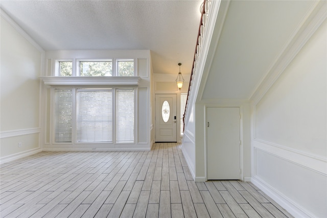 foyer entrance with ornamental molding, light hardwood / wood-style flooring, and a textured ceiling