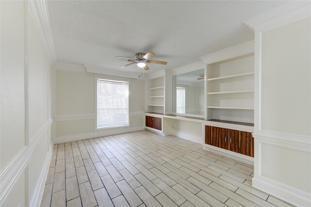 spare room featuring light hardwood / wood-style flooring, ornamental molding, a textured ceiling, built in shelves, and ceiling fan