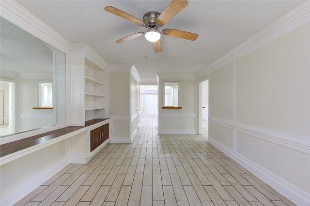 spare room with ornamental molding, built in shelves, light hardwood / wood-style floors, and ceiling fan