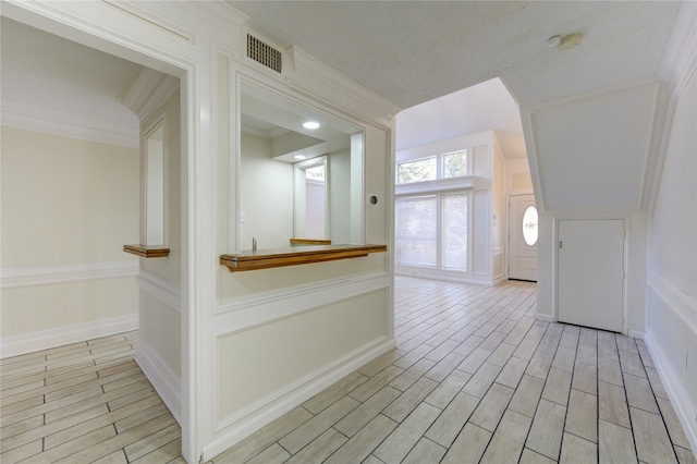 hall featuring ornamental molding, a textured ceiling, and light hardwood / wood-style floors