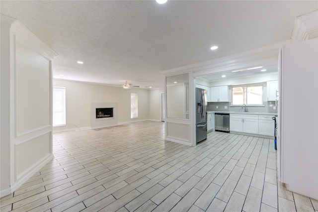 unfurnished living room with ceiling fan, crown molding, sink, and light wood-type flooring