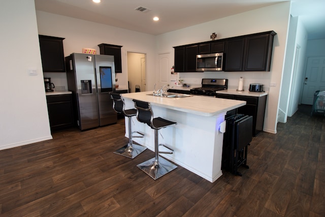 kitchen featuring appliances with stainless steel finishes, dark wood-type flooring, an island with sink, a breakfast bar area, and sink