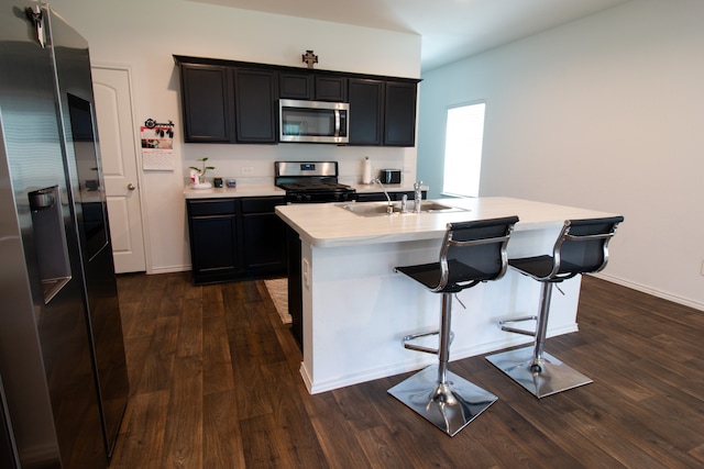 kitchen featuring appliances with stainless steel finishes, an island with sink, a breakfast bar area, dark hardwood / wood-style flooring, and sink