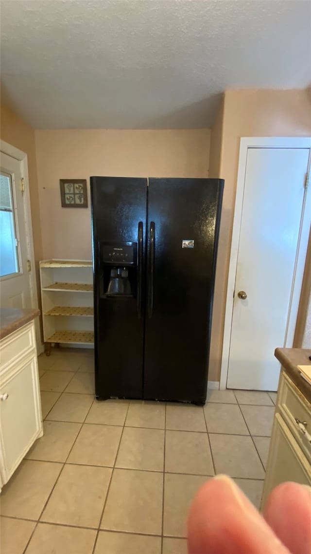 kitchen featuring black fridge, light tile patterned floors, and white cabinetry