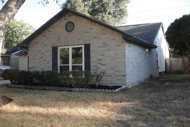 view of property exterior featuring a yard, brick siding, roof with shingles, and fence