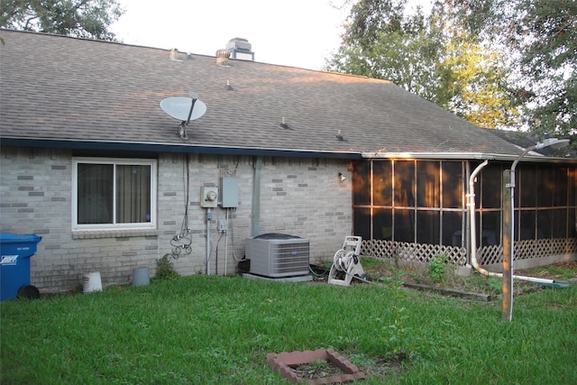 back of property featuring central air condition unit, a sunroom, roof with shingles, and a yard