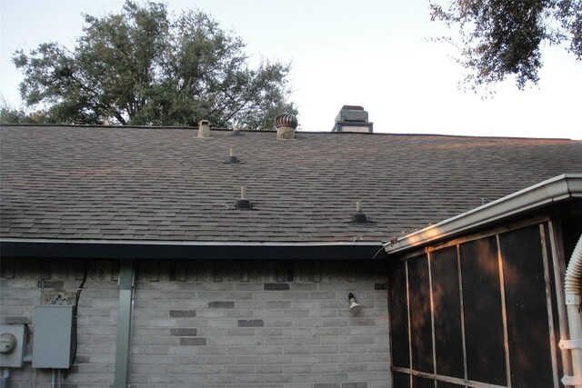 details featuring stone siding, a shingled roof, and electric meter