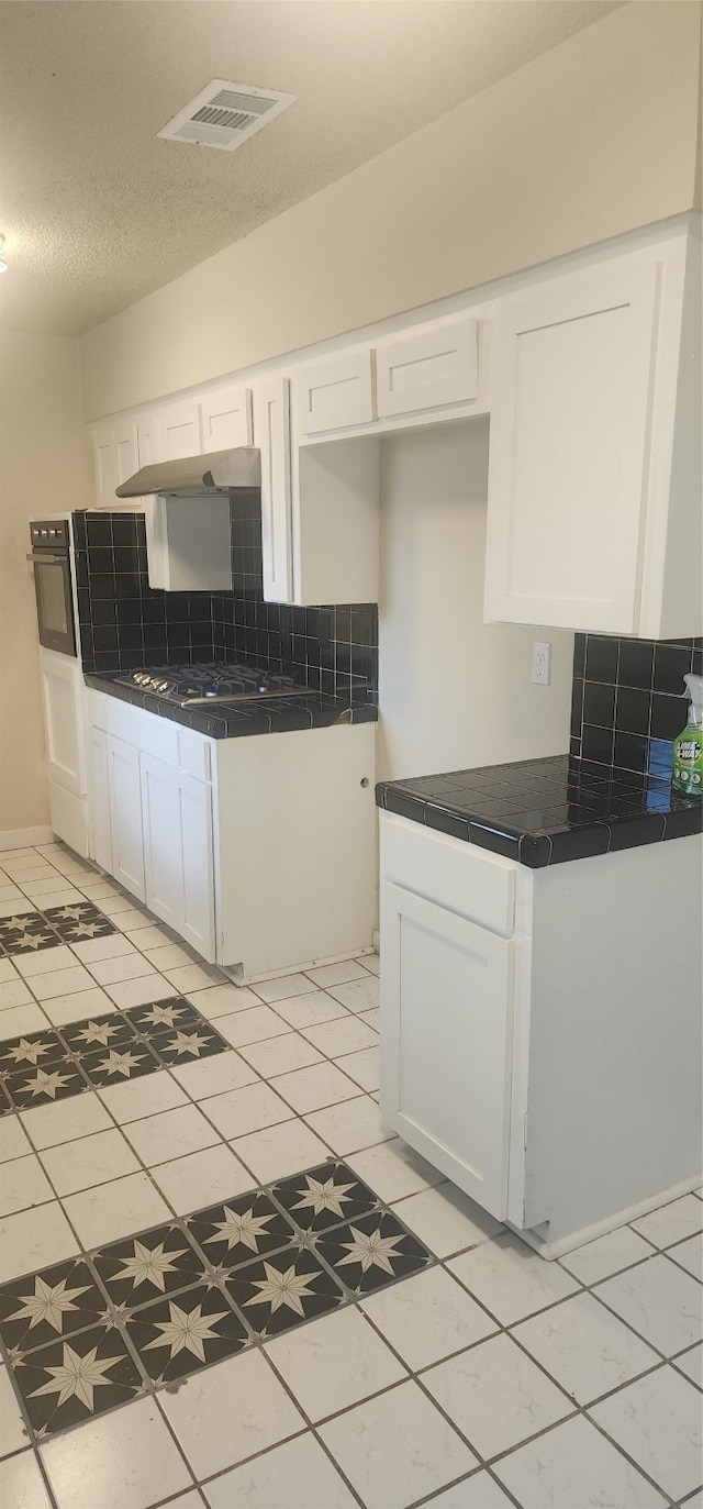 kitchen with a textured ceiling, backsplash, light tile patterned floors, and white cabinets