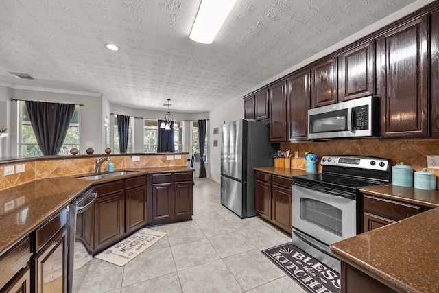 kitchen with light tile patterned floors, a sink, dark brown cabinets, appliances with stainless steel finishes, and decorative light fixtures