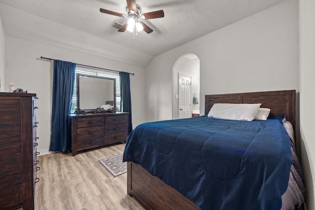 bedroom with a textured ceiling, arched walkways, visible vents, vaulted ceiling, and light wood finished floors