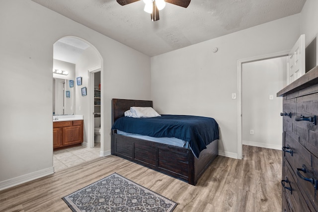 bedroom featuring arched walkways, light wood-type flooring, baseboards, and ensuite bathroom