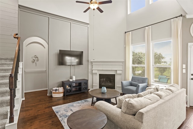 living room with a towering ceiling, ceiling fan, plenty of natural light, and dark wood-type flooring