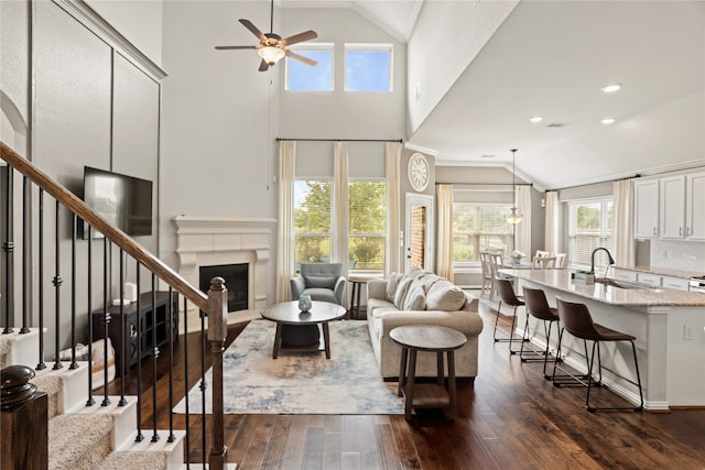 living room with dark hardwood / wood-style flooring, sink, ceiling fan with notable chandelier, high vaulted ceiling, and crown molding