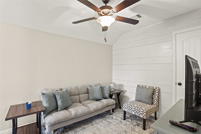 living room featuring ceiling fan, wood walls, and vaulted ceiling