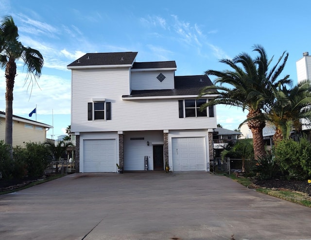 view of front of house with driveway, stone siding, a garage, and fence