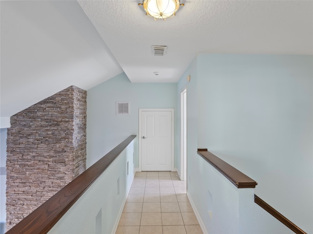 corridor with a textured ceiling, vaulted ceiling, and light tile patterned floors