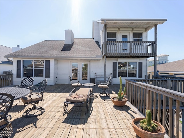 rear view of property with a balcony, a chimney, a deck, roof with shingles, and french doors