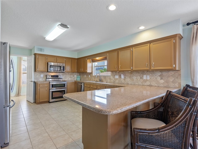 kitchen featuring a breakfast bar area, kitchen peninsula, stainless steel appliances, light tile patterned floors, and a textured ceiling