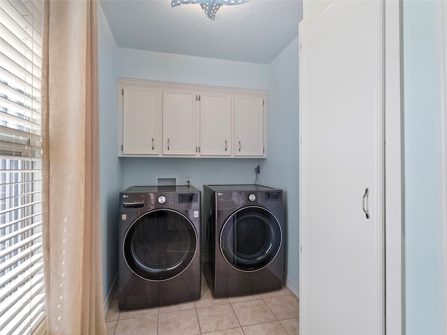 laundry room featuring light tile patterned flooring, a textured ceiling, cabinets, and washing machine and clothes dryer