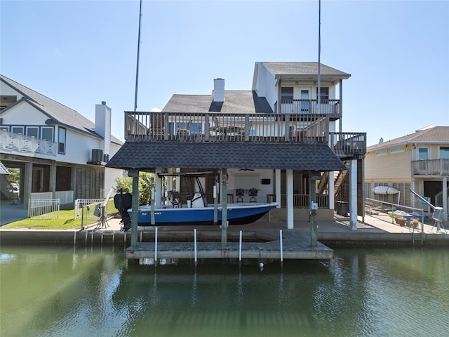 rear view of property featuring cooling unit, a deck with water view, boat lift, and roof with shingles