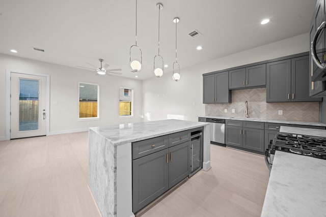 kitchen featuring gray cabinetry, sink, light stone countertops, pendant lighting, and light wood-type flooring