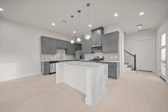 kitchen with gray cabinets, a center island, appliances with stainless steel finishes, and decorative backsplash