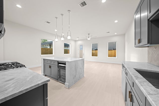 kitchen with beverage cooler, light stone counters, light hardwood / wood-style flooring, gray cabinets, and a center island