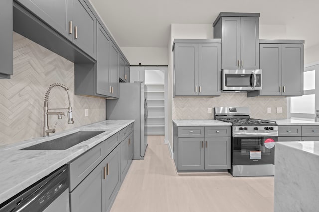 kitchen with light stone countertops, stainless steel appliances, sink, and gray cabinetry