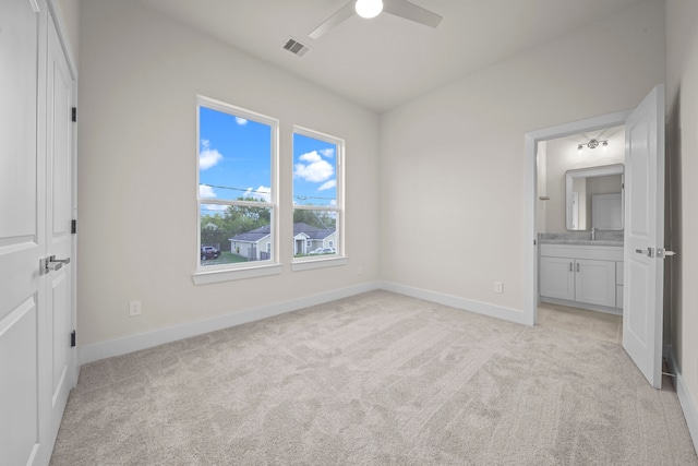 unfurnished bedroom featuring ceiling fan, ensuite bathroom, and light colored carpet